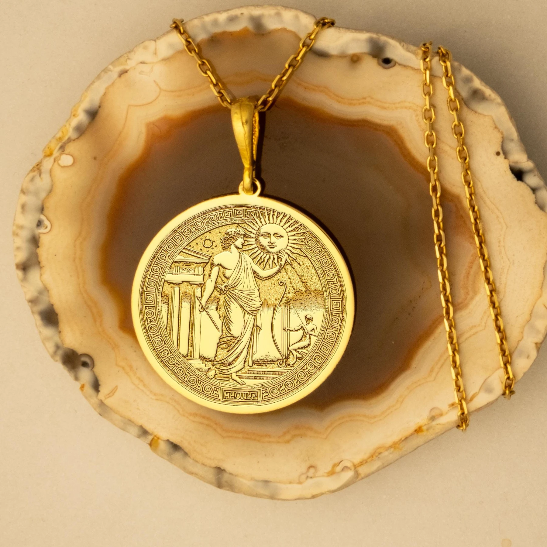 Luxe Amulet Apollo gold medallion necklace displayed on a natural agate surface