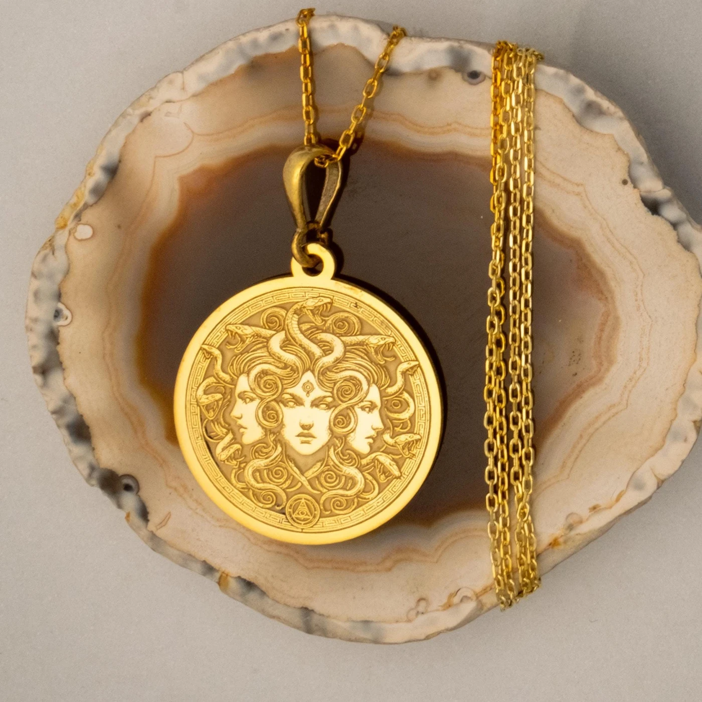 Luxe Amulet Medusa gold medallion necklace displayed on a natural agate surface