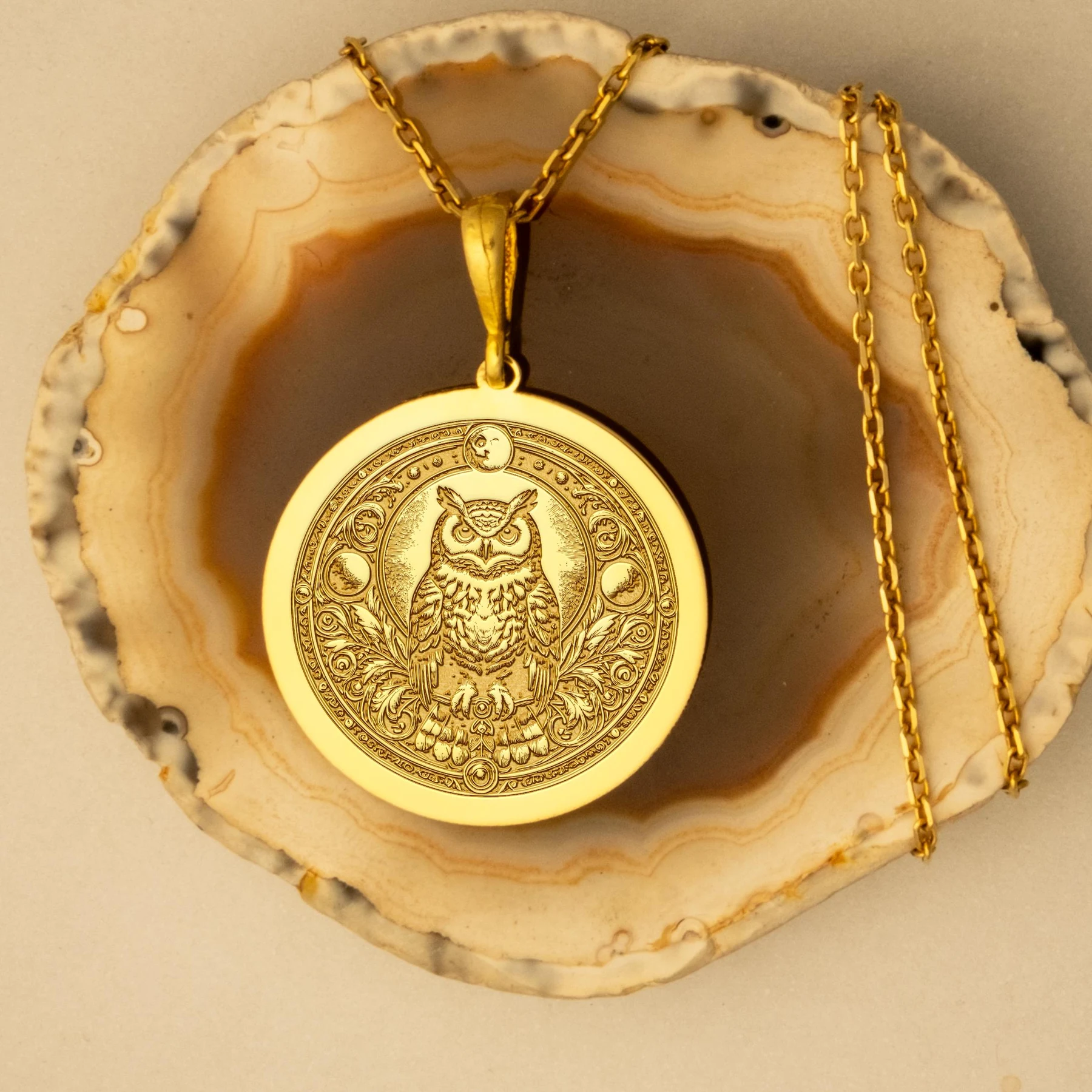 Luxe Amulet gold owl medallion displayed on a natural agate surface